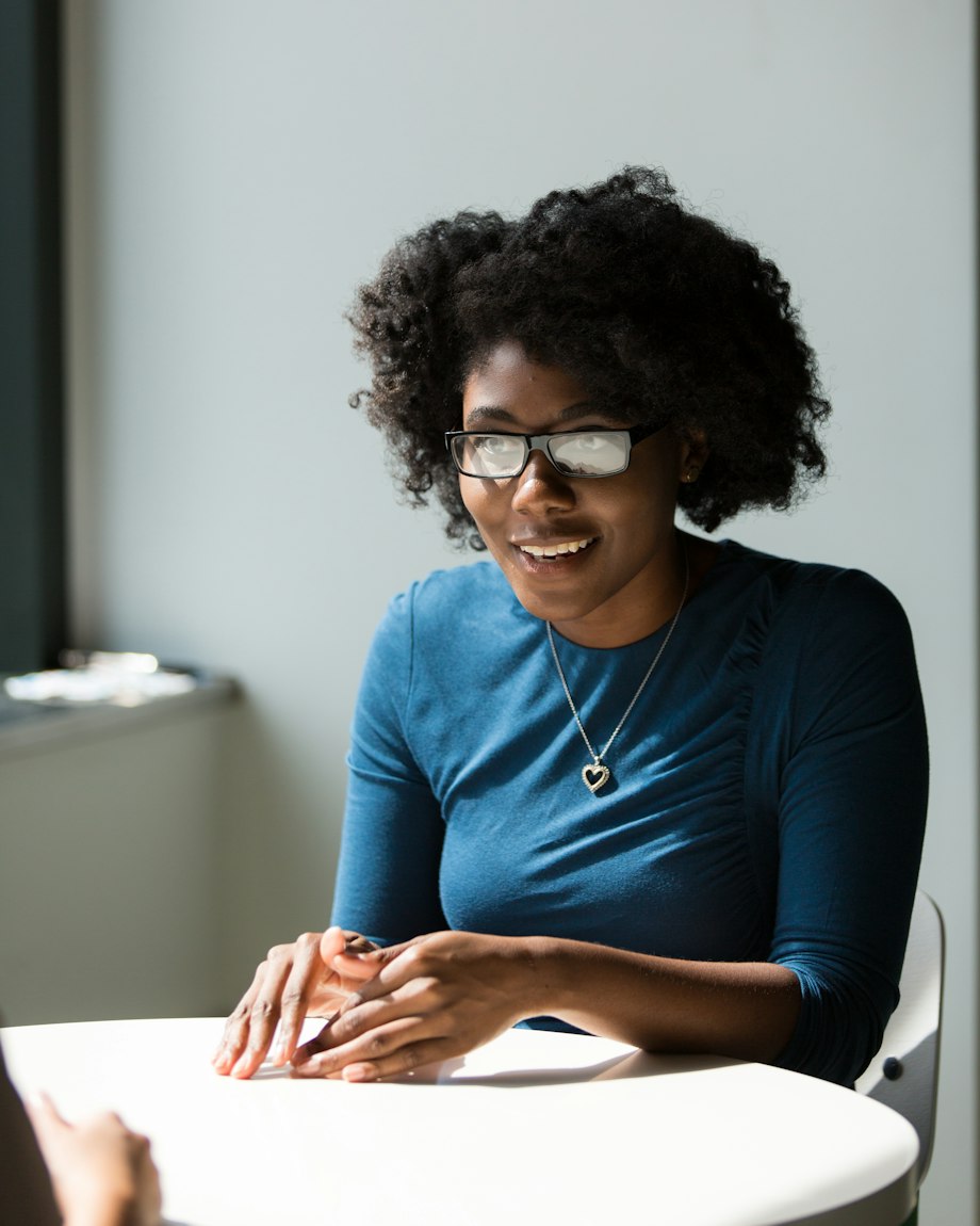 Mulher sorrindo durante uma conversa, sentada a uma mesa